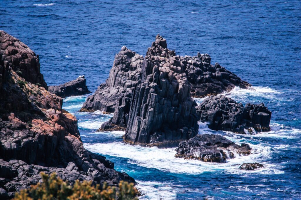 dolerite rock formations sticking out from the sea with white sea spray