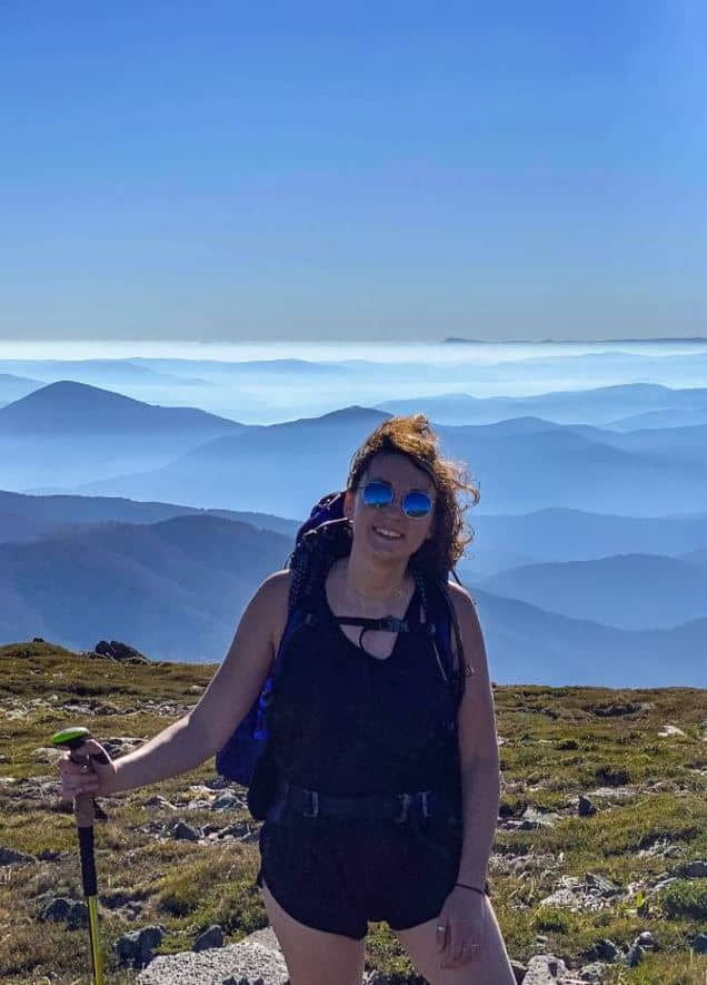 solo woman standing on top of a mountain with cloud covered mountain range in the background